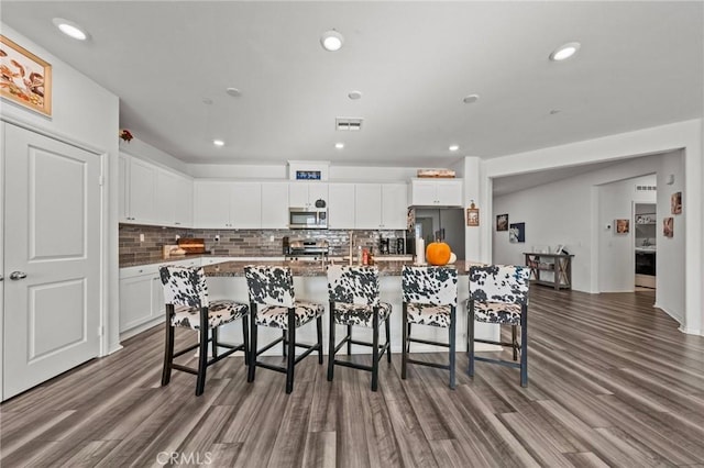 kitchen with tasteful backsplash, a kitchen bar, white cabinets, stainless steel appliances, and a kitchen island with sink