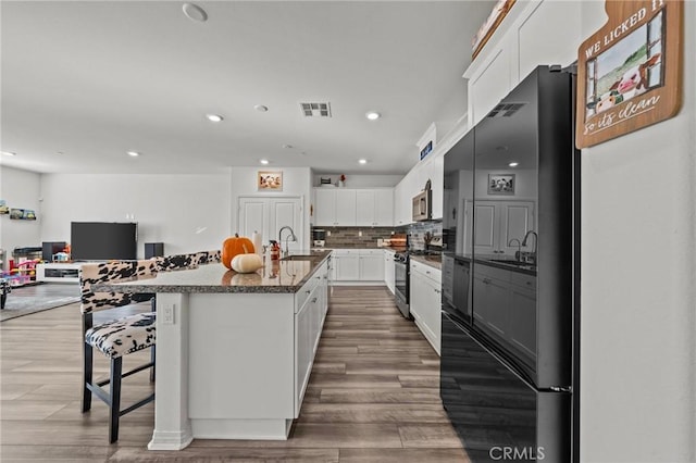 kitchen with visible vents, decorative backsplash, appliances with stainless steel finishes, wood finished floors, and white cabinetry