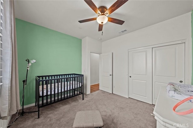 carpeted bedroom featuring visible vents, a crib, baseboards, a closet, and a ceiling fan