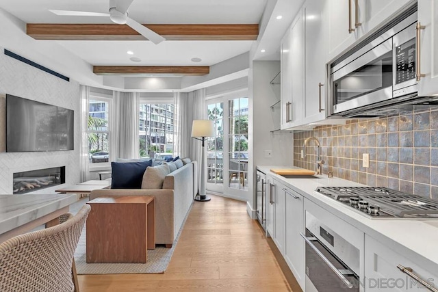 kitchen featuring white cabinetry, light wood-type flooring, beamed ceiling, sink, and stainless steel appliances