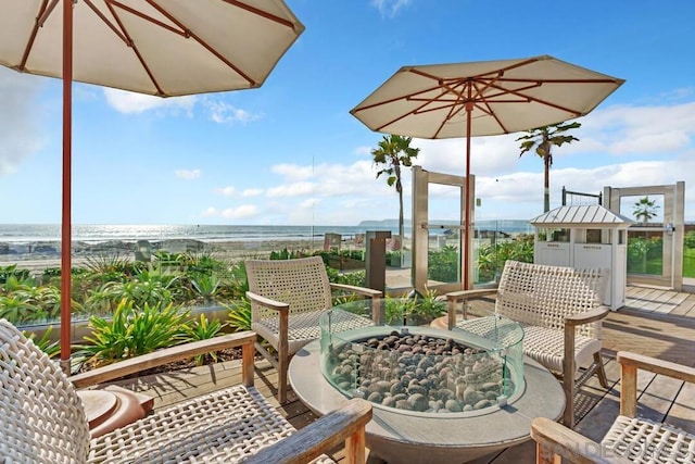 balcony featuring a deck with water view, a fire pit, and a view of the beach