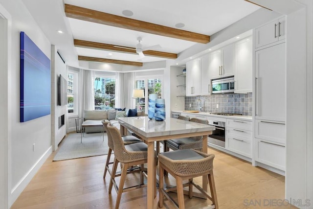 kitchen featuring beamed ceiling, light hardwood / wood-style flooring, white cabinets, and stainless steel appliances