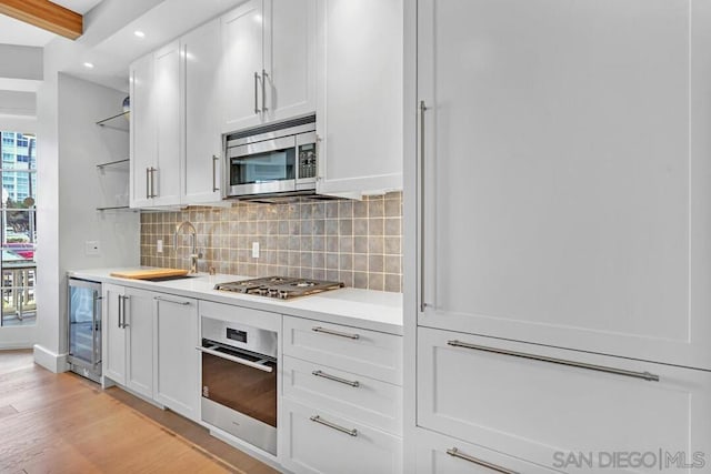 kitchen with appliances with stainless steel finishes, white cabinets, beverage cooler, and light wood-type flooring