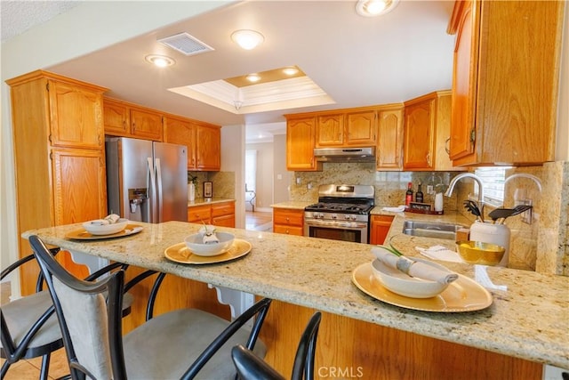 kitchen featuring kitchen peninsula, appliances with stainless steel finishes, ornamental molding, a raised ceiling, and a breakfast bar area