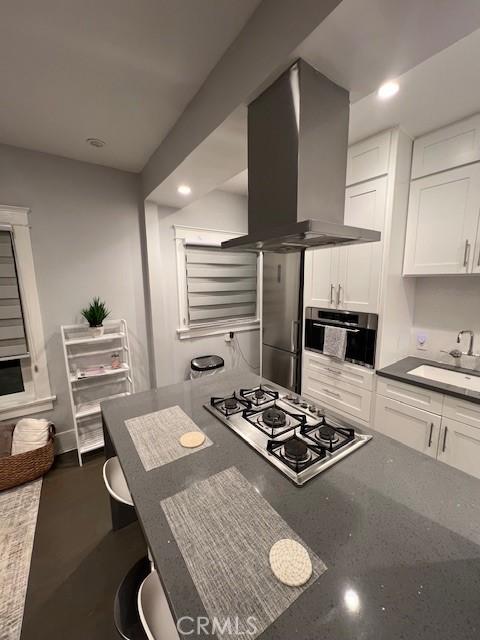 kitchen featuring white cabinets, wall chimney range hood, sink, and appliances with stainless steel finishes