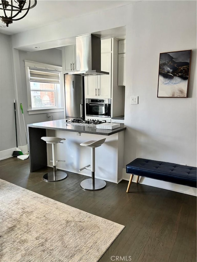 kitchen featuring wall chimney exhaust hood, dark hardwood / wood-style flooring, a breakfast bar, white cabinets, and appliances with stainless steel finishes