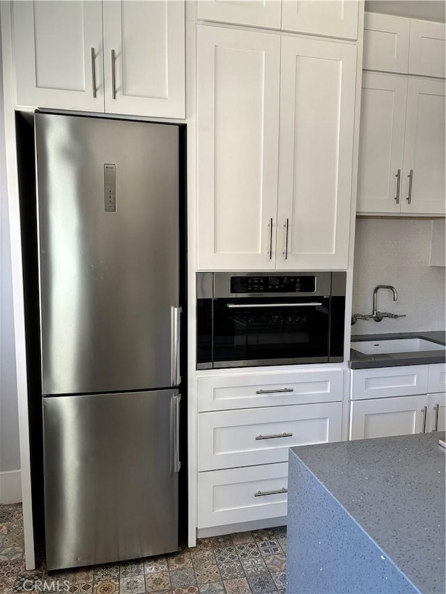 kitchen with light stone counters, sink, white cabinets, and appliances with stainless steel finishes