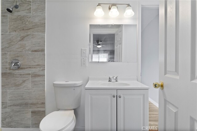 bathroom featuring tiled shower, hardwood / wood-style flooring, toilet, vanity, and ceiling fan