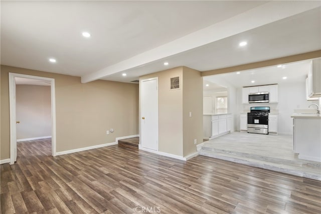 unfurnished living room featuring beam ceiling, sink, and light hardwood / wood-style floors