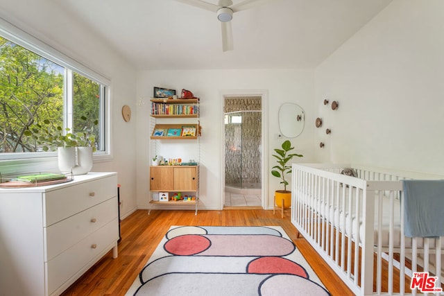 bedroom with ensuite bathroom, light hardwood / wood-style flooring, ceiling fan, and a crib