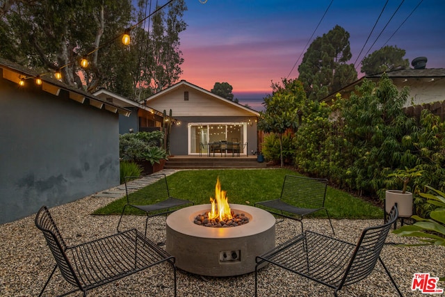 back house at dusk with a fire pit and a lawn