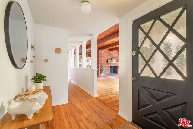 foyer entrance featuring beam ceiling, decorative columns, light hardwood / wood-style flooring, and a brick fireplace