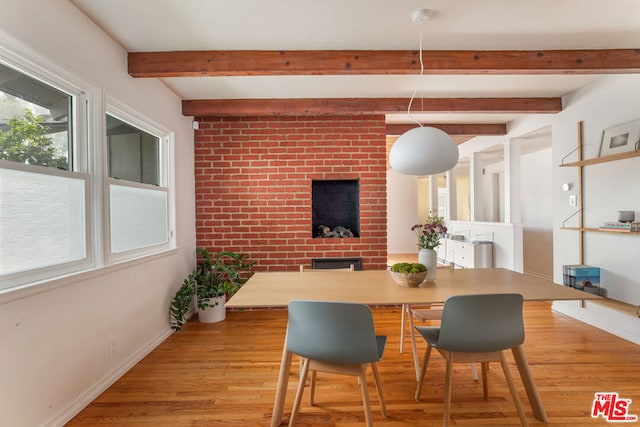 dining room featuring beamed ceiling, light hardwood / wood-style floors, and a brick fireplace