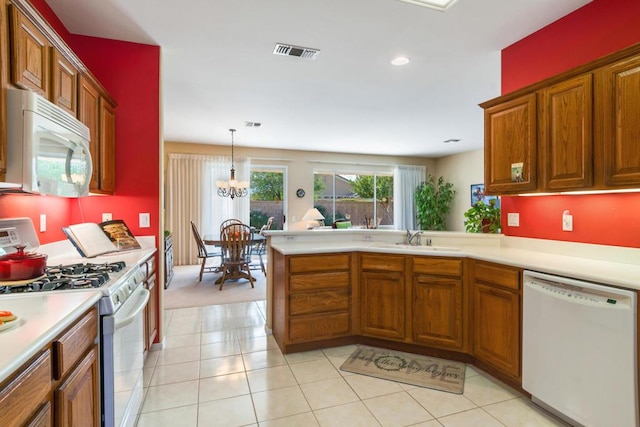 kitchen with a notable chandelier, kitchen peninsula, sink, white appliances, and hanging light fixtures