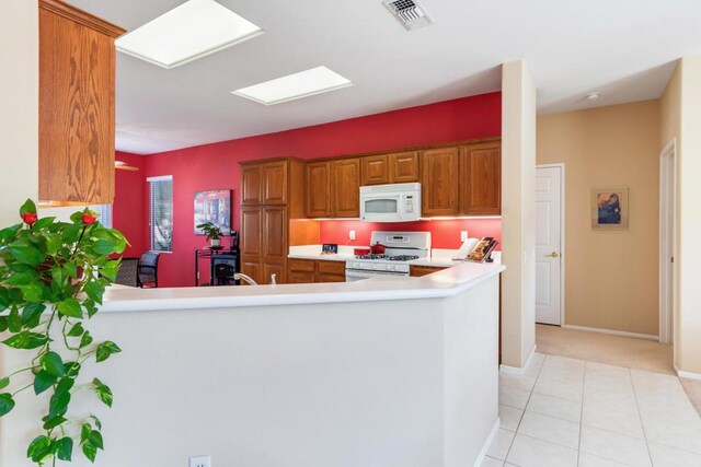 kitchen featuring white appliances, light tile patterned floors, and kitchen peninsula