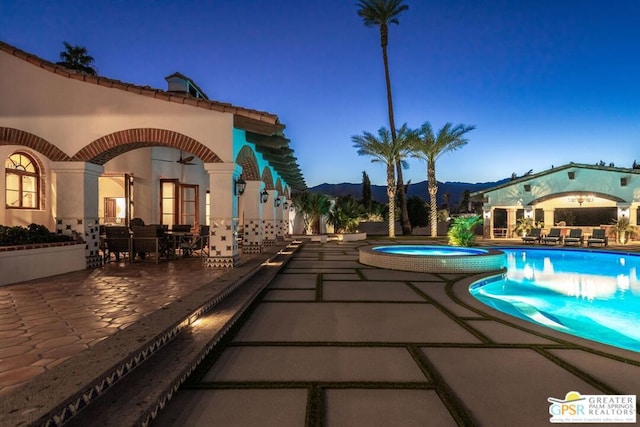 pool at dusk with a mountain view, an in ground hot tub, and a patio