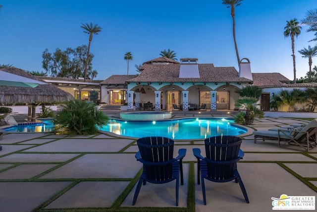 pool at dusk featuring a patio area and an in ground hot tub