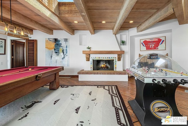 game room featuring hardwood / wood-style flooring, pool table, beamed ceiling, wood ceiling, and a tiled fireplace