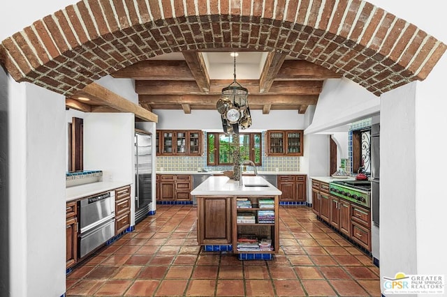 kitchen with sink, a kitchen island with sink, a chandelier, decorative backsplash, and appliances with stainless steel finishes