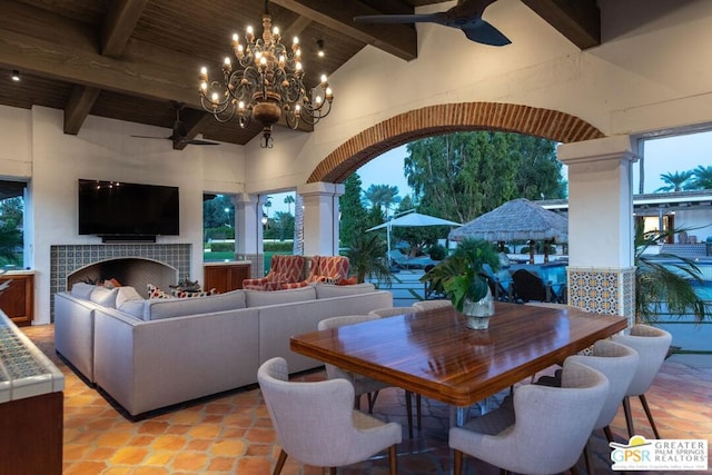 interior space featuring beamed ceiling, high vaulted ceiling, a tiled fireplace, wood ceiling, and ceiling fan with notable chandelier