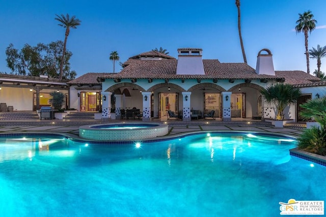 pool at dusk featuring a grill, a patio area, and an in ground hot tub