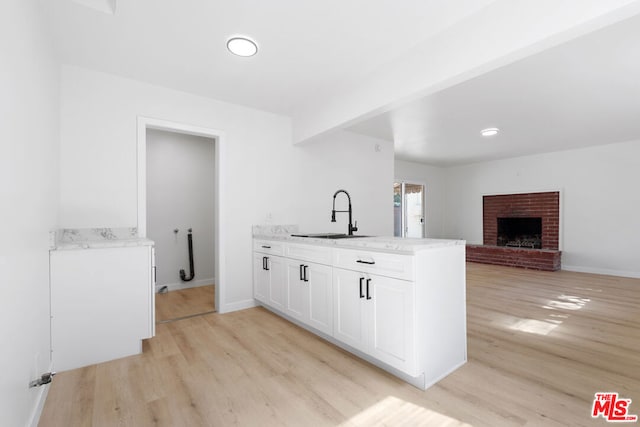 kitchen featuring sink, kitchen peninsula, a fireplace, white cabinets, and light wood-type flooring