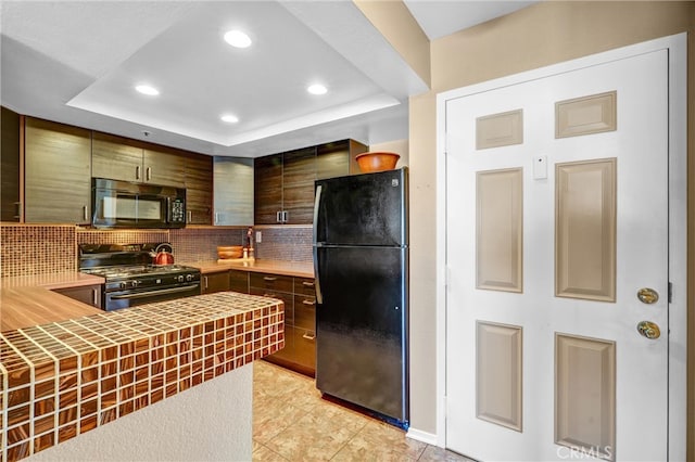 kitchen featuring tasteful backsplash, black appliances, light tile patterned floors, and a raised ceiling