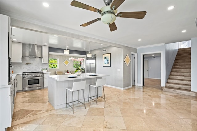 kitchen featuring a kitchen island with sink, wall chimney range hood, high end range, ornamental molding, and pendant lighting