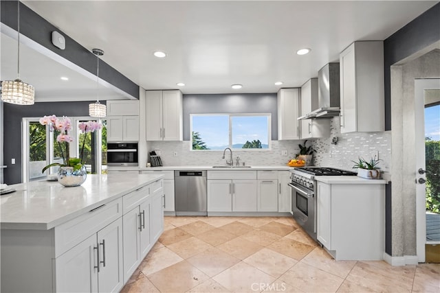 kitchen with appliances with stainless steel finishes, white cabinetry, decorative light fixtures, and wall chimney range hood