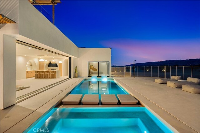 pool at dusk featuring a patio area, a bar, and a hot tub