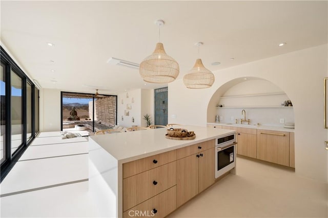 kitchen with stainless steel oven, sink, hanging light fixtures, light brown cabinetry, and a kitchen island