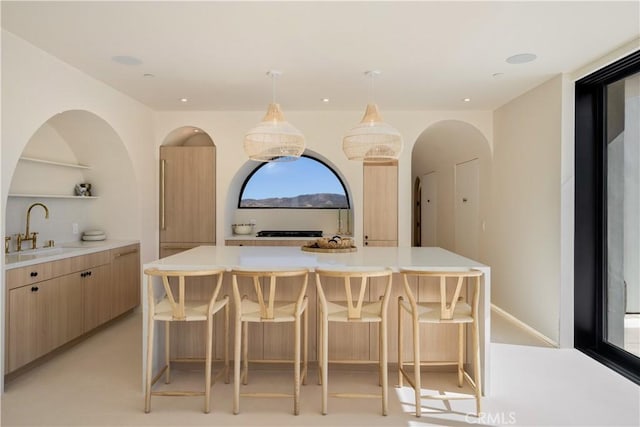 bar featuring sink, decorative light fixtures, and light brown cabinets