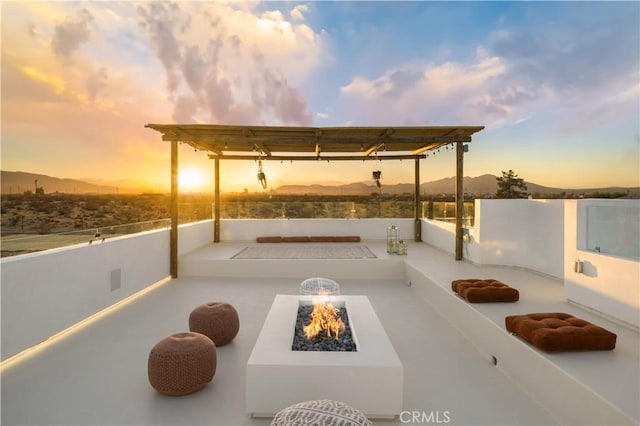 patio terrace at dusk with a mountain view, a pergola, and an outdoor fire pit