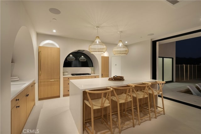 kitchen with light brown cabinetry, a center island, and pendant lighting