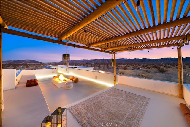 patio terrace at dusk featuring a fire pit, a mountain view, and a pergola