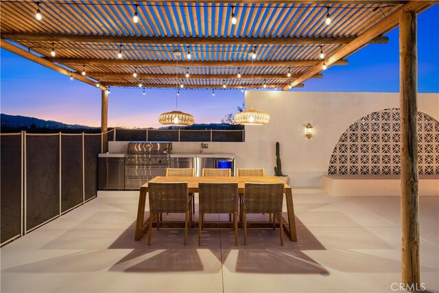 patio terrace at dusk featuring an outdoor kitchen, a grill, and a pergola