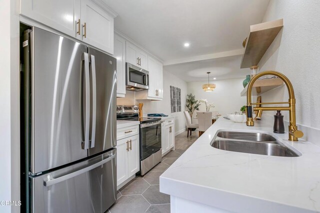 kitchen featuring light stone counters, stainless steel appliances, sink, white cabinetry, and hanging light fixtures