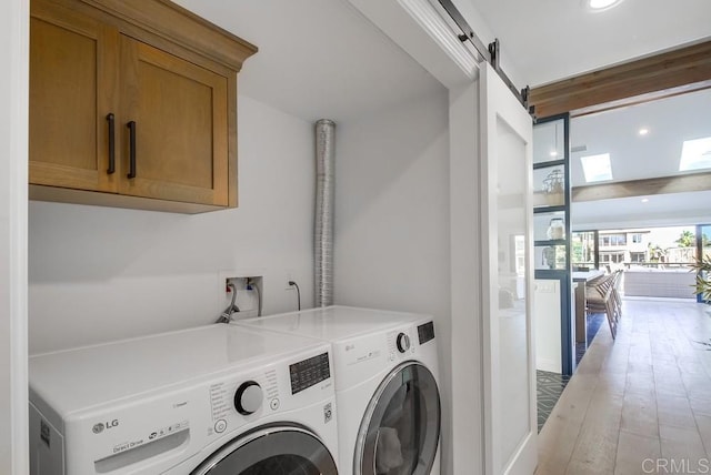 51 Catspaw, Coronado, CA 92118 - clothes washing area featuring washer and clothes dryer, a barn door, light wood-style floors, and cabinet space