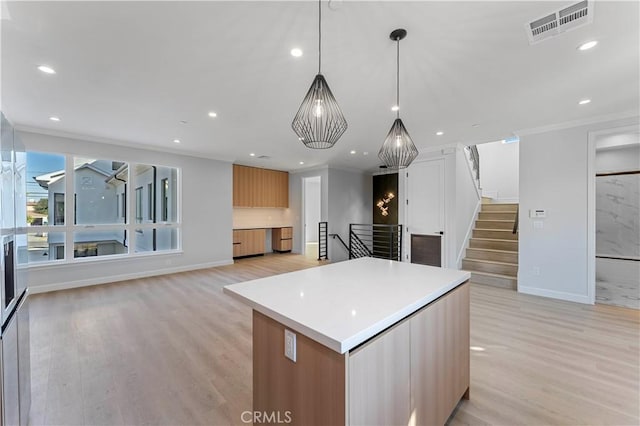 kitchen with decorative light fixtures, a kitchen island, ornamental molding, and light hardwood / wood-style flooring