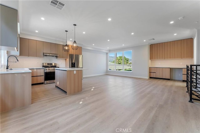 kitchen with appliances with stainless steel finishes, sink, decorative light fixtures, light hardwood / wood-style floors, and a kitchen island