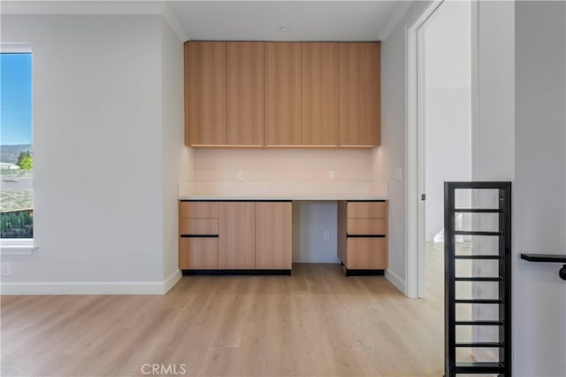 kitchen with light brown cabinets, built in desk, ornamental molding, and light wood-type flooring