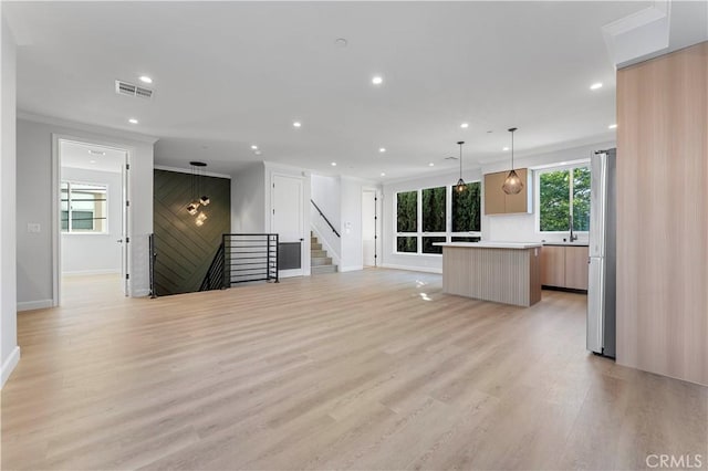 unfurnished living room with light wood-type flooring, sink, and ornamental molding