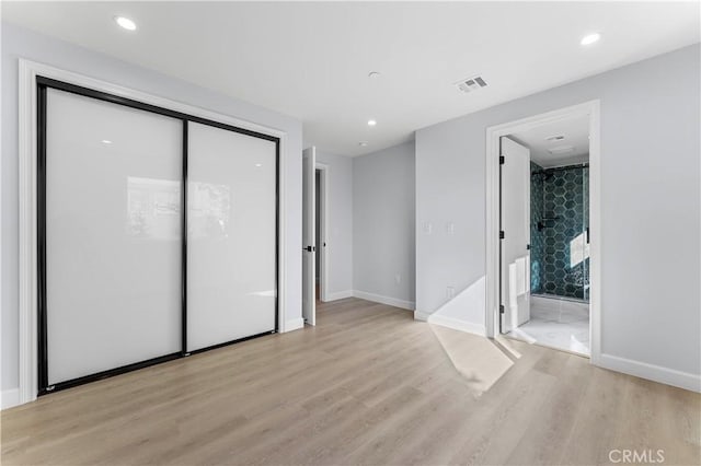 unfurnished bedroom with ensuite bathroom, a closet, and light wood-type flooring