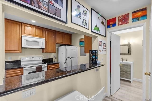 kitchen with light hardwood / wood-style floors, dark stone counters, and white appliances