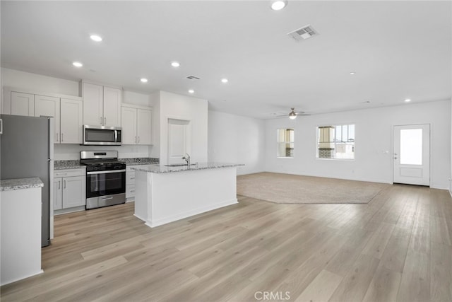 kitchen with light hardwood / wood-style floors, appliances with stainless steel finishes, light stone counters, and white cabinets