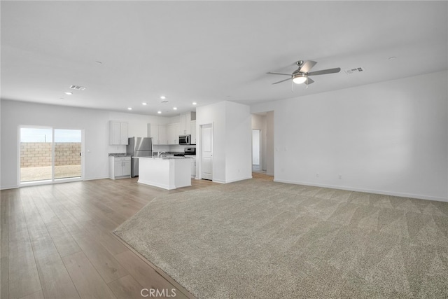 unfurnished living room featuring sink, light wood-type flooring, and ceiling fan