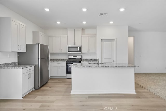 kitchen with white cabinetry, light stone counters, stainless steel appliances, and an island with sink