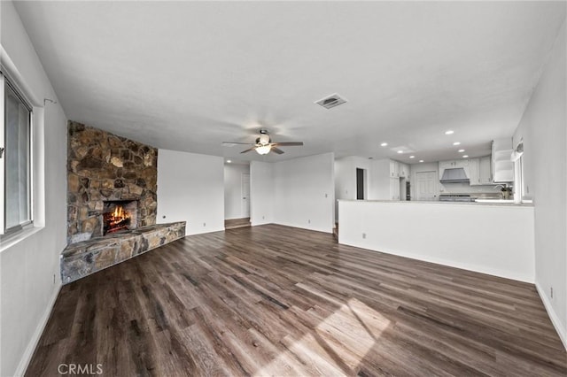 unfurnished living room with ceiling fan, a stone fireplace, and dark hardwood / wood-style flooring