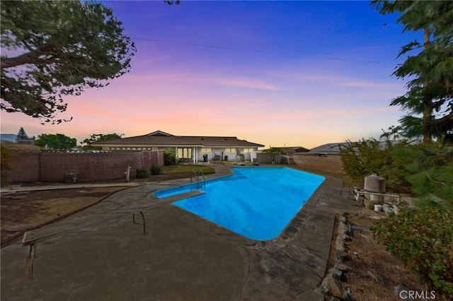 pool at dusk featuring a patio area and a diving board