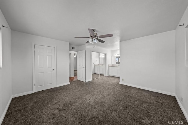 unfurnished bedroom featuring ensuite bathroom, dark carpet, and ceiling fan